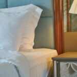 Elegant close-up of a comfortable bedroom setup with white linens and a decorative lamp.