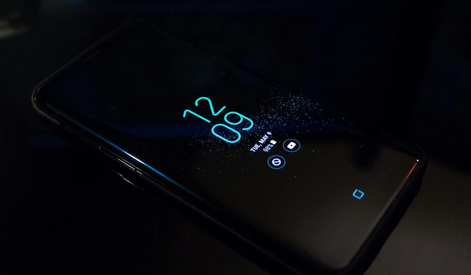 Close-up of a smartphone in the dark displaying digital clock and notifications.