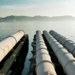 Sewage pipes stretch over a tranquil waterfront in Lisbon, highlighting urban infrastructure.