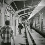 Busy train station platform captured in black and white, featuring commuters boarding and disembarking.