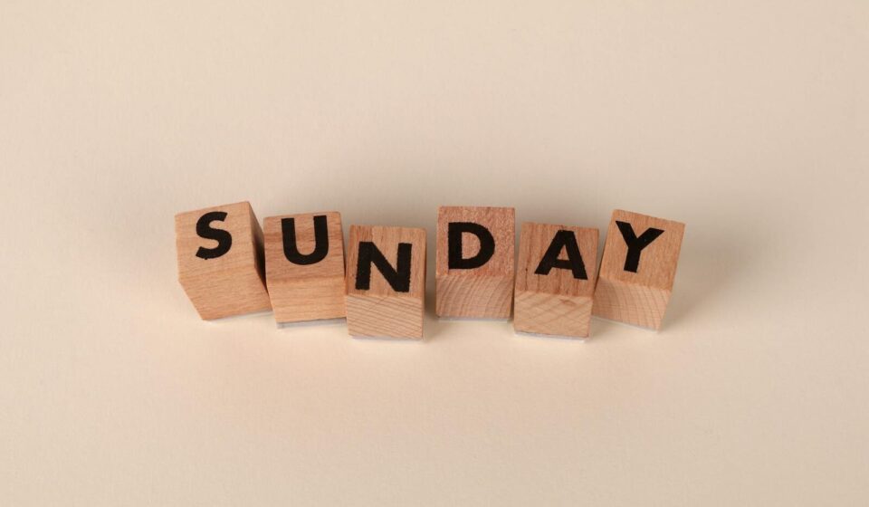 Wooden letter blocks spelling 'Sunday' on a neutral background for weekend concepts.