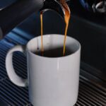 Close-up of espresso machine brewing fresh coffee into a white mug in a cafe setting.
