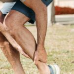 Adult male grabbing ankle due to injury in outdoor setting, wearing rubber running shoes.