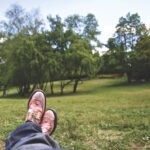 A person relaxes in a lush green park, feet up, enjoying a sunny day.