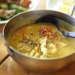 A close-up of a flavorful Thai chicken curry served in a metal bowl with fresh herbs.