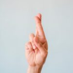 Close-up of a hand with fingers crossed against a light blue background symbolizing hope or luck.