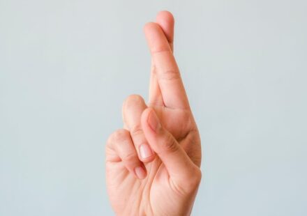 Close-up of a hand with fingers crossed against a light blue background symbolizing hope or luck.