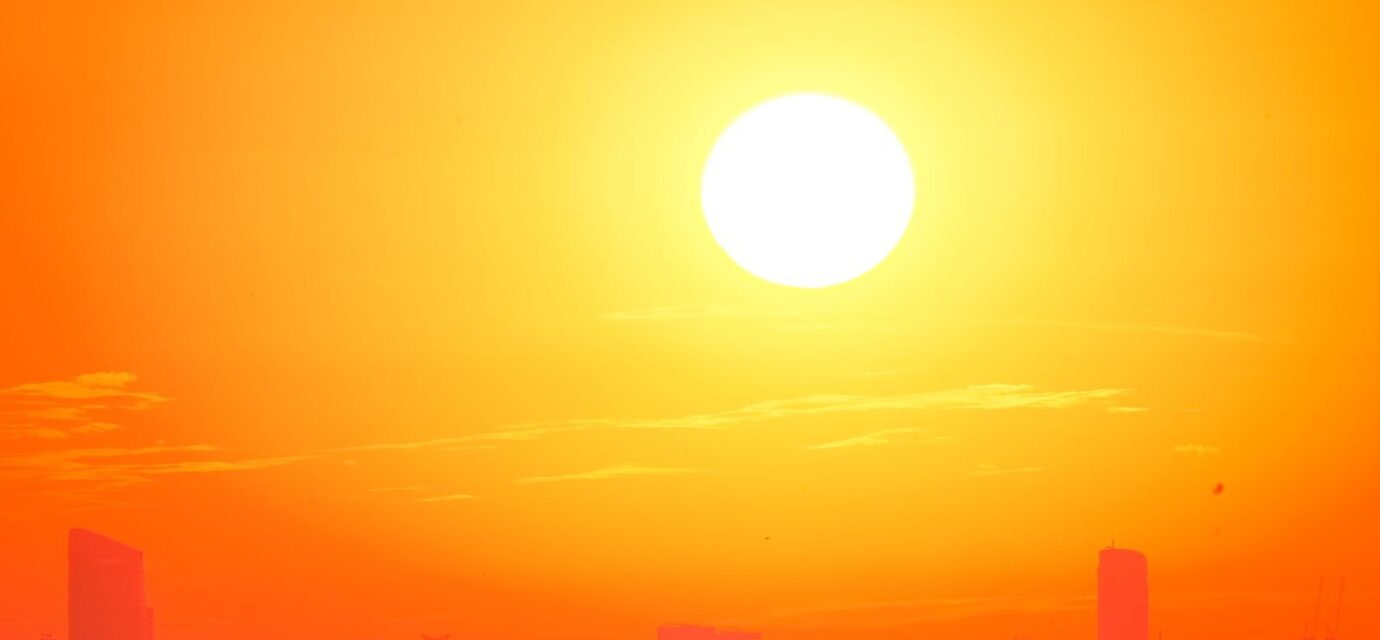 A city skyline silhouetted against a vivid, orange sunset sky.