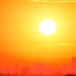 A city skyline silhouetted against a vivid, orange sunset sky.