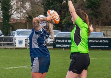 A rugby player prepares a throw-in while a referee signals with a flag during a match.