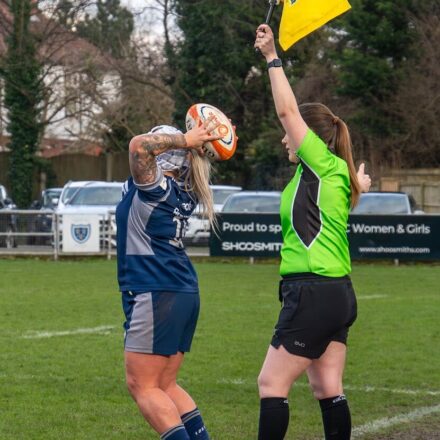 A rugby player prepares a throw-in while a referee signals with a flag during a match.