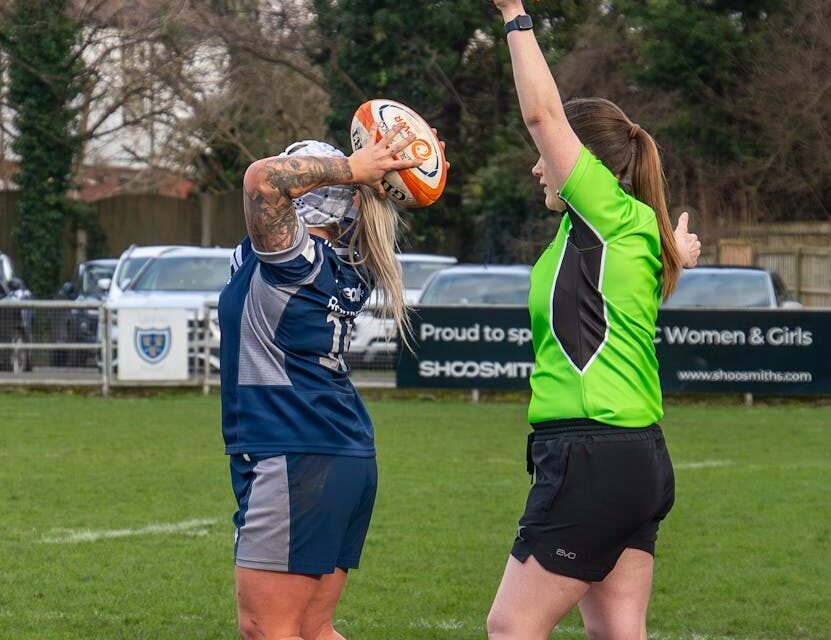 A rugby player prepares a throw-in while a referee signals with a flag during a match.